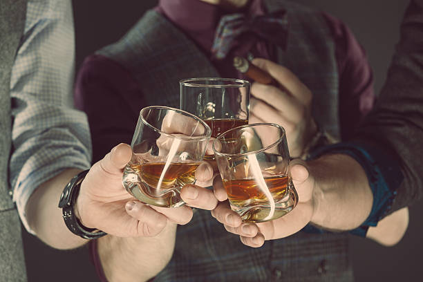 Three men drinking whiskey. Close up of glasses and hands. Dark tone.