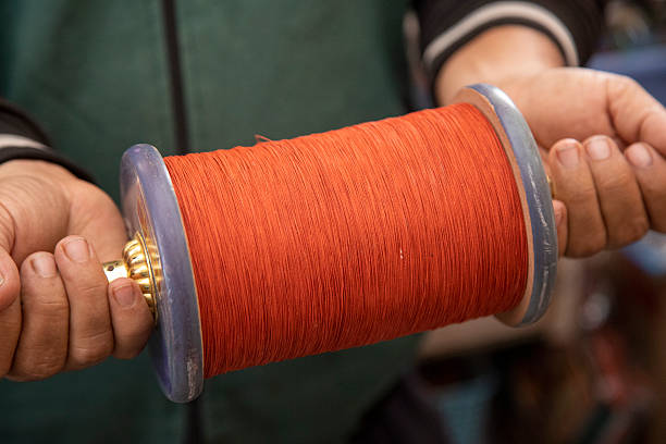 A man holds a charkhi (phirki) thread spool in the crook of his elbow while winding it with the other hand, preparing for the vibrant kite-fighting festivities of Makar Sankranti or Uttarayana in India.